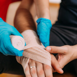 Arm being bandaged first aid gloves in care setting being worn by first aider